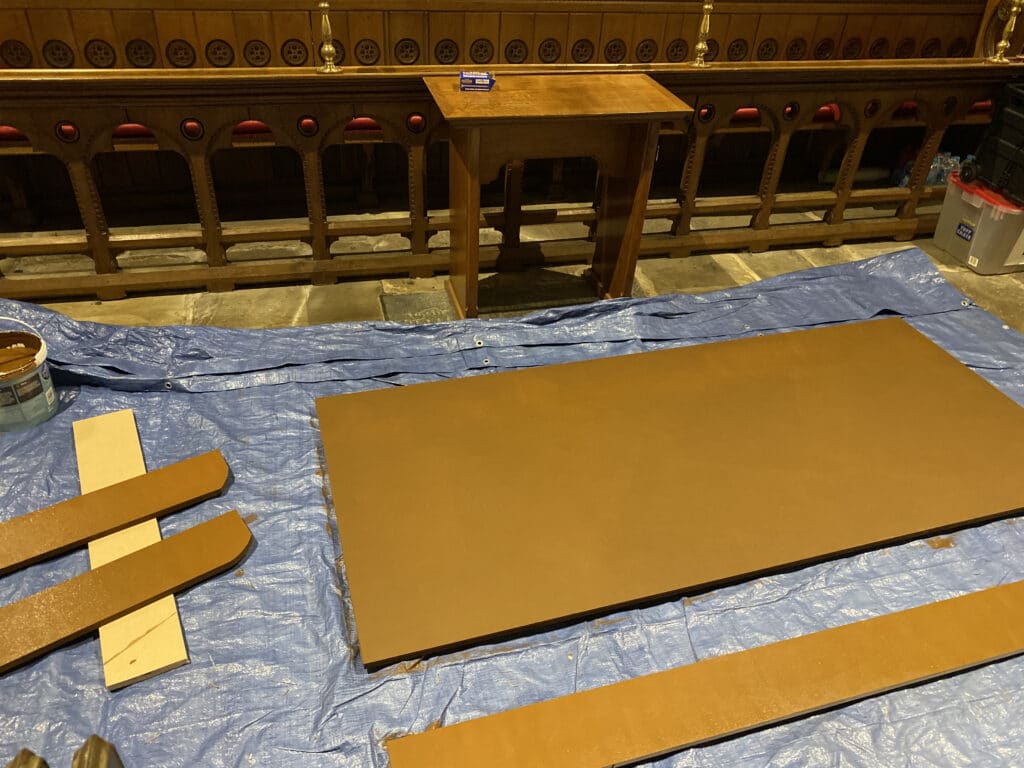 Parts of wood lying on a tarpaulin on the church floor, waiting for woodstain to dry
